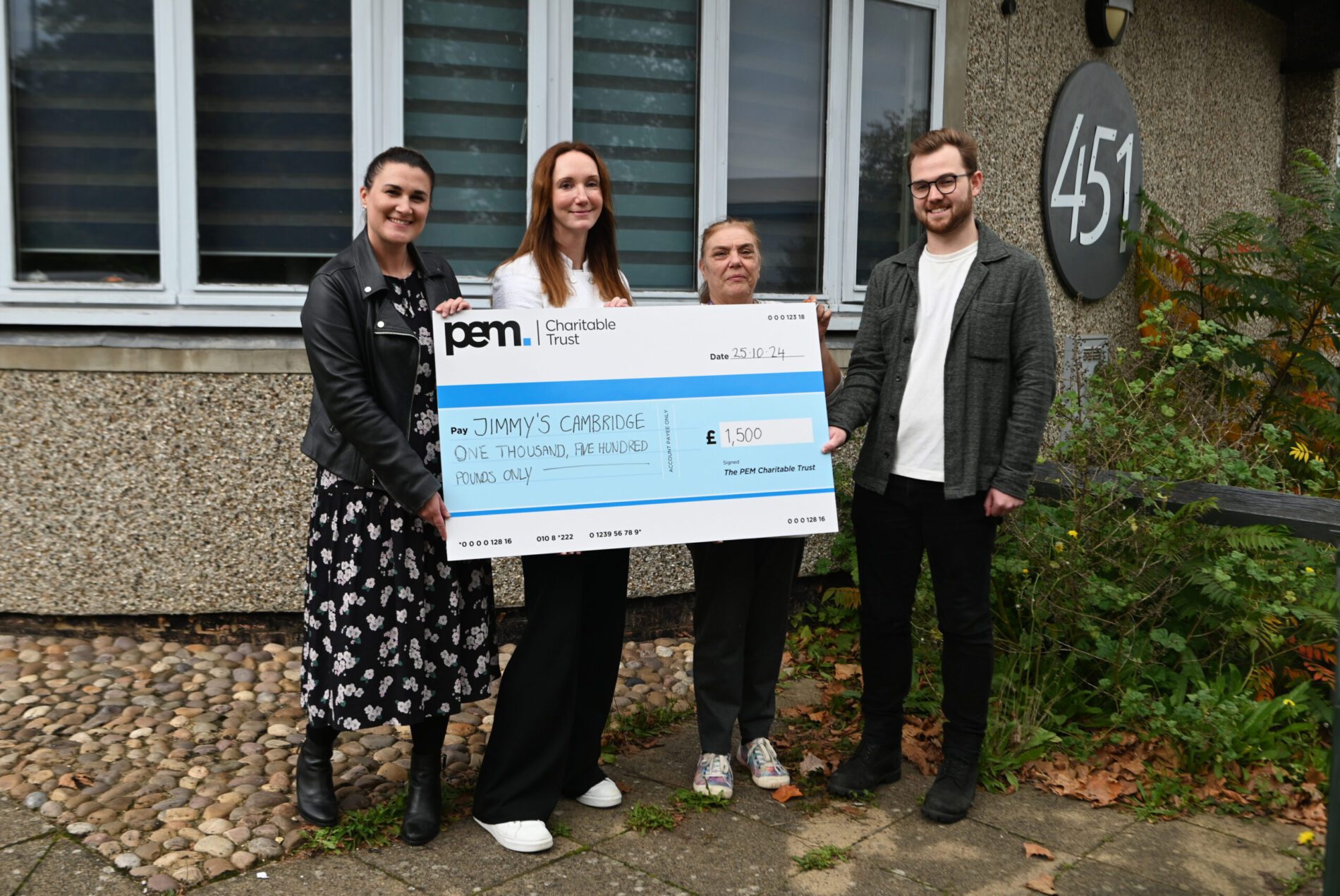 Jimmy's Cambridge charity donation from PEM. Three women and one man stand behind PEM branded large novelty cheque for £1500.