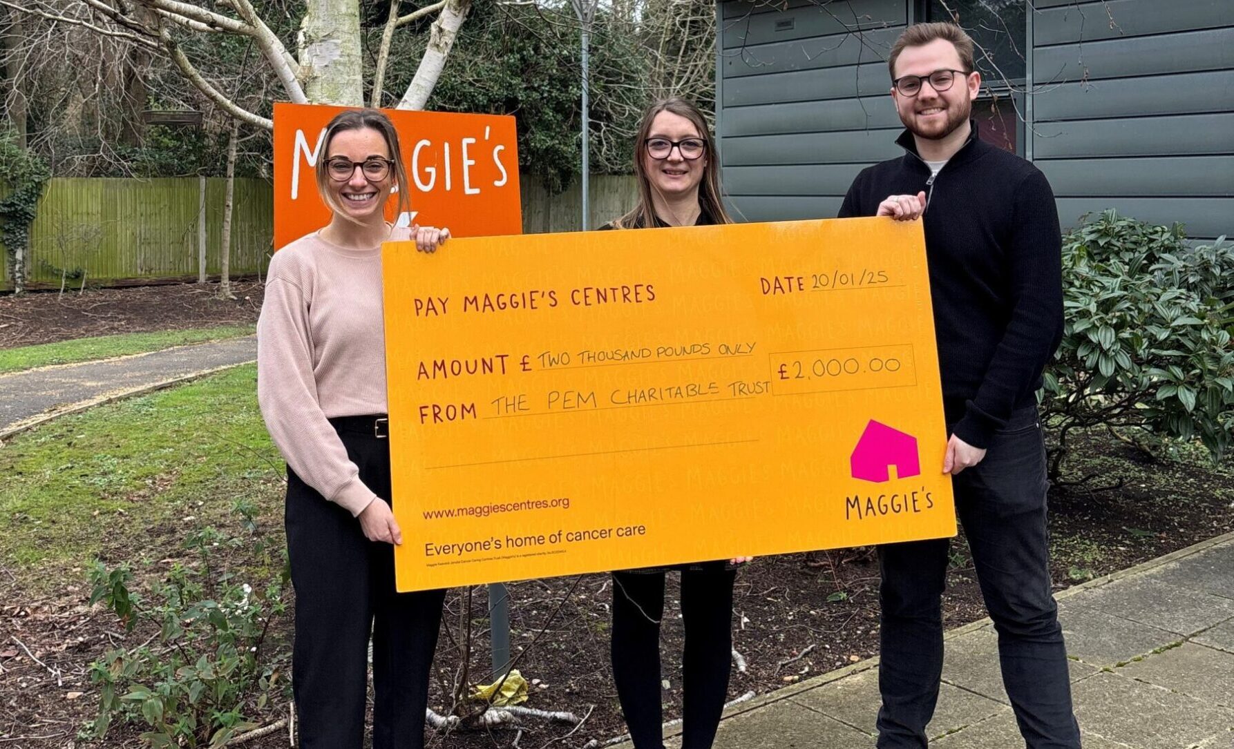 Three people holding large orange cheque for a donation of £2000 to Maggie's charity from the PEM Charitable Trust