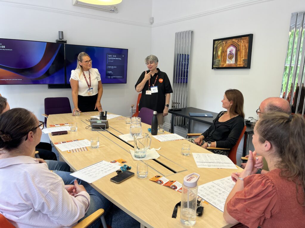 people in meeting room sat around a table during a training session with two trainers standing up