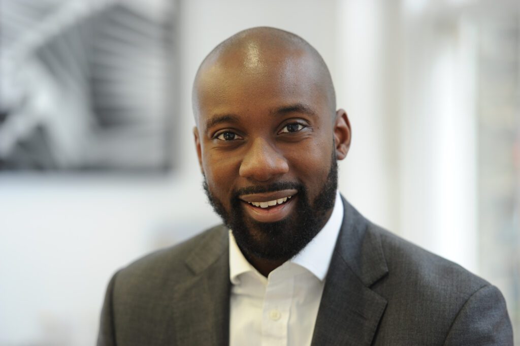 Head shot photo of a black man, Philip, smiling and wearing a suit