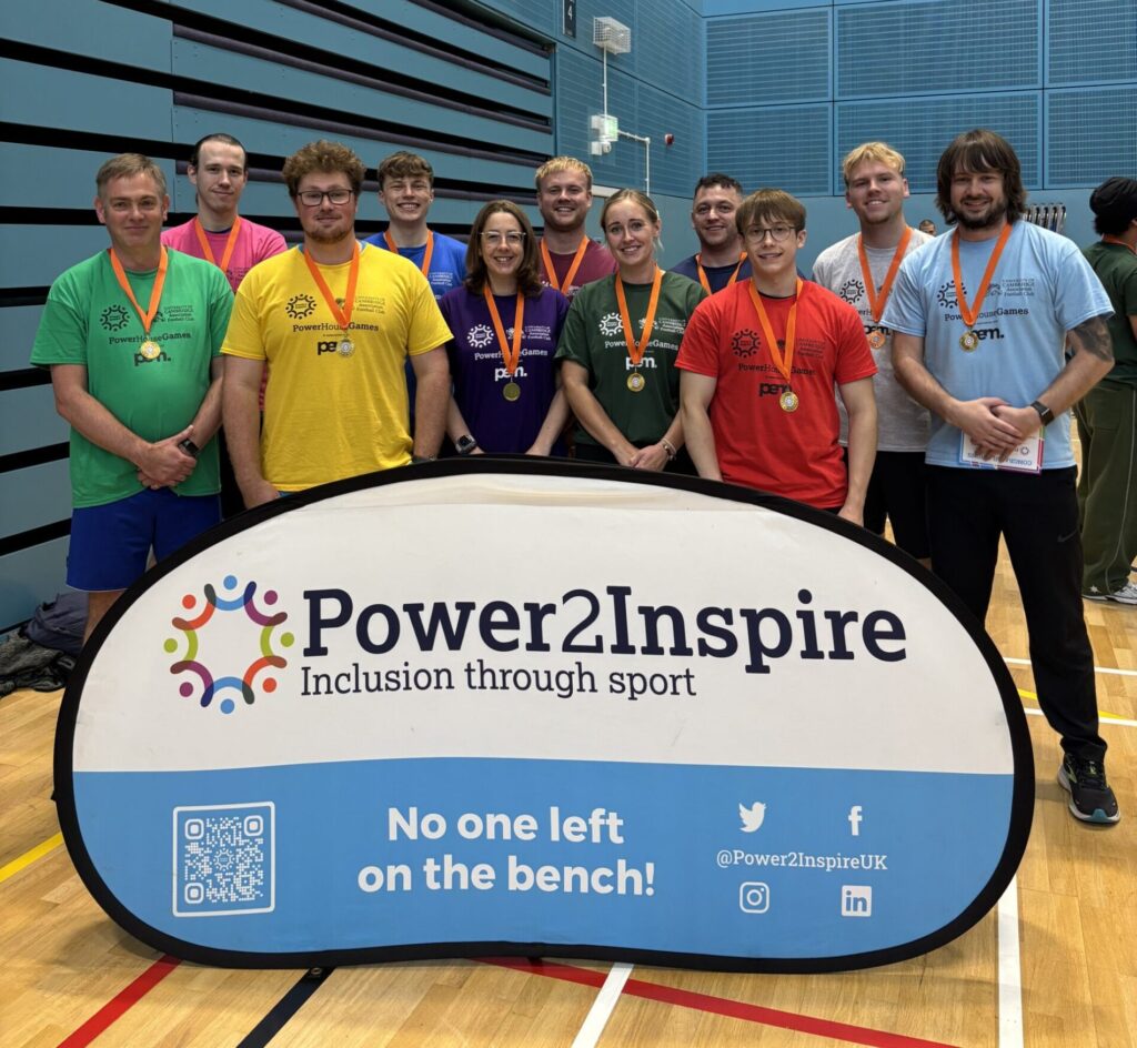 People istood behind a power 2 inspire sign, all in different coloured sports tops, in a sports hall